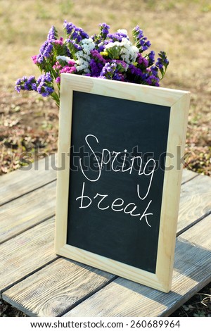 Spring break concept. Beautiful wild flowers in vase and frame on wooden table outdoors
