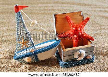 Toy model of ship with wooden box and starfish on sea sand background