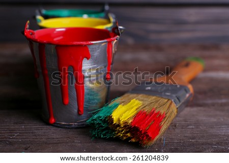 Metal buckets with colorful paint near brush on wooden background