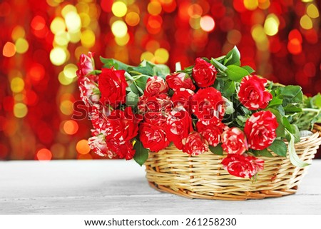 Beautiful roses in wicker basket on table on bright background
