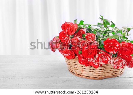 Beautiful roses in wicker basket on table on light background