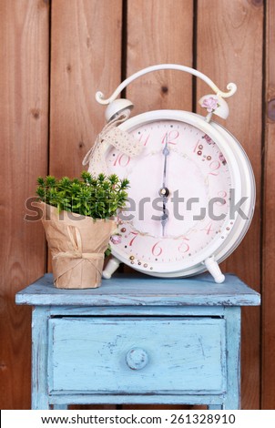 Interior design with big alarm clock and plant on tabletop on wooden planks background