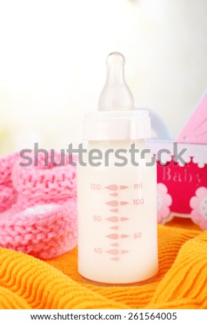 Baby milk bottle, pacifier and babys bootees on yellow background