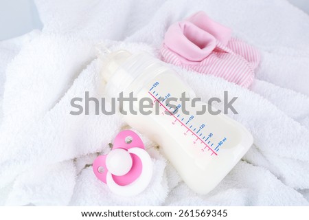 Baby milk bottle, pacifier and babys bootees on towel