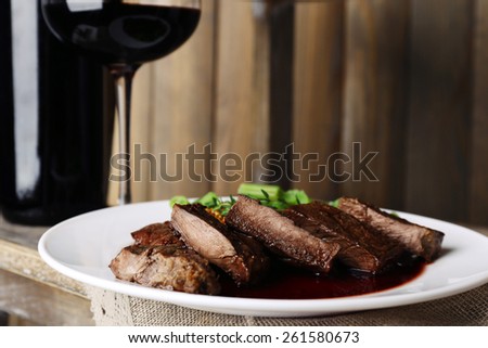 Steak with wine sauce on plate and bottle of wine on wooden background