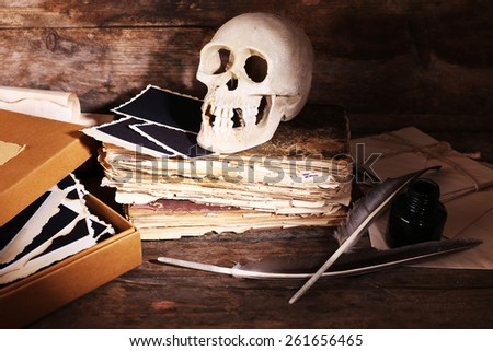 Still life with human skull, retro book and quill on wooden background