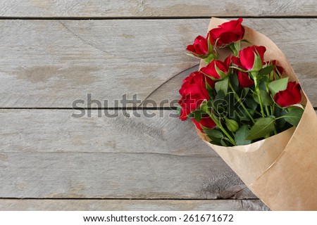 Red roses wrapped in paper on wooden table background