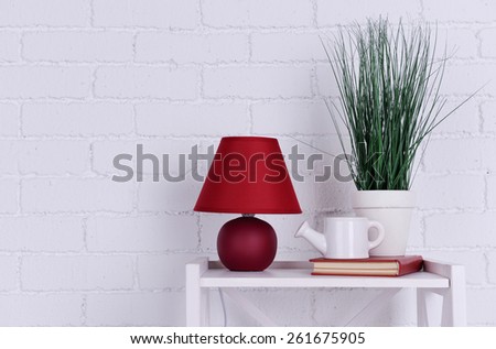 Interior design with lamp, plant, ceramic watering pot and book on tabletop on white brick wall background