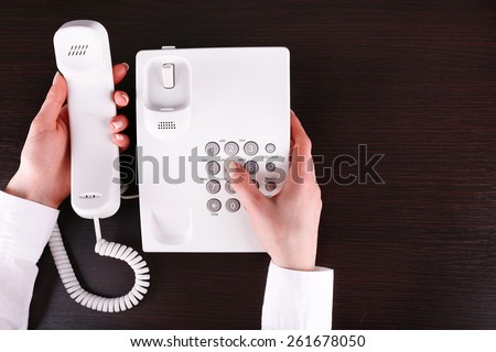 Female hand holding phone receiver and dialing number on wooden background