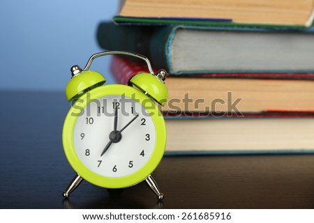 Stack of books with alarm clock on wooden desk and colorful background