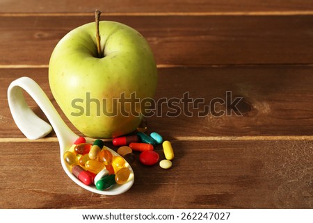 Apple and colorful pills, on wooden background