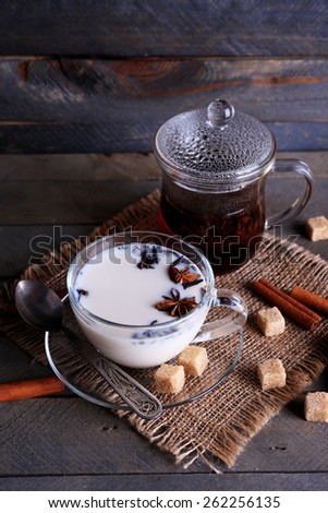 Black tea with milk in glassware and lump sugar on color wooden planks background