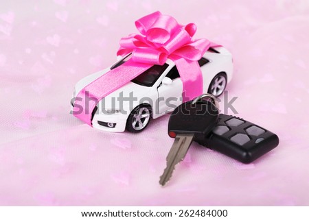 Keys and car with bow as present on pink background