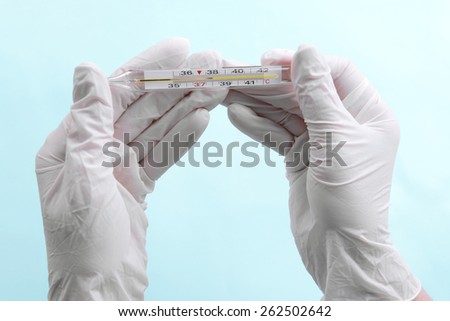 Hands with gloves holding thermometer on blue background