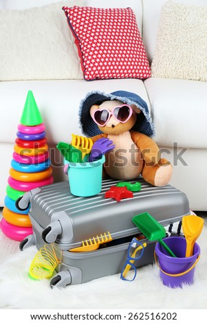 Suitcase packed with clothes and child toys on fur rug and white sofa background