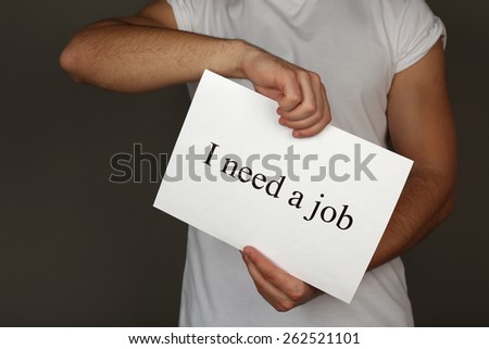 Sheet of paper with inscription I need a job in male hands on dark background