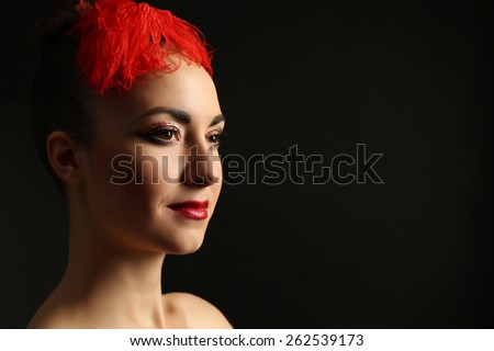 Portrait of beautiful woman with fancy glitter makeup and red feather on dark background