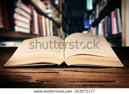 Open book on table on bookshelves background
