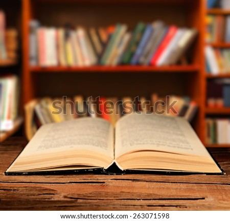 Open book on table on bookshelves background