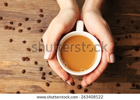 Female hands holding cup with coffee beans on wooden table background