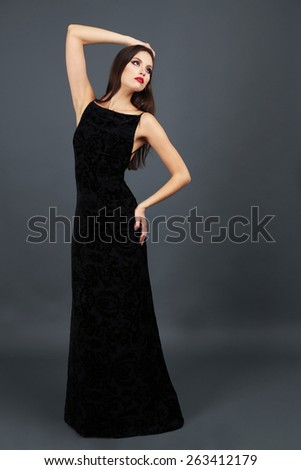 Beautiful young woman in long black dress on dark gray background