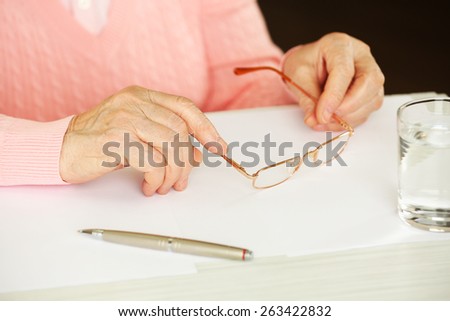 Hands of adult woman with pen, glasses and glass of water on table, on dark background