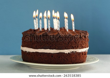 Delicious chocolate cake with candles on table on blue background