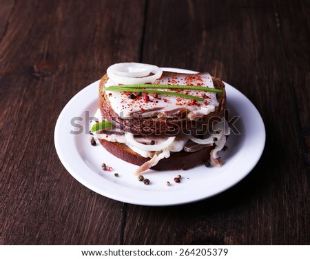 Sandwiches with lard and onion on plate on wooden background