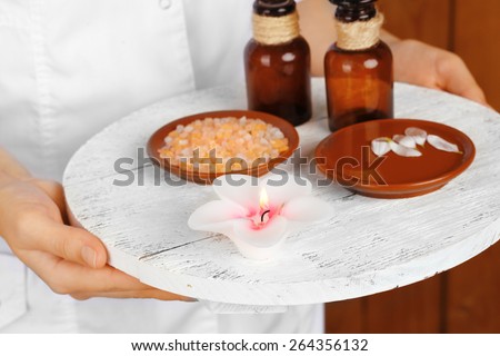 Beauty therapist holding tray of spa treatments, close-up, on wooden wall background