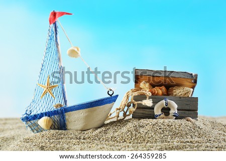 Marine still life with toy model of ship on sand on blue background