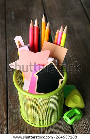 Colorful pencils with paper notes in metal stand on wooden table background