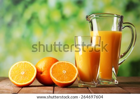 Glass and pitcher of orange juice on wooden table on natural background