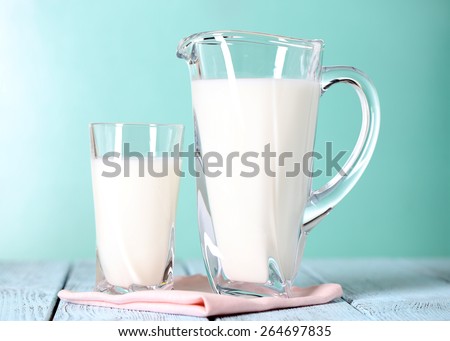 Pitcher and glass of milk on wooden table on blue background