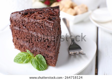Piece of delicious chocolate cake with mint in plate with fork on color wooden table background