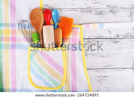 Set of kitchen utensils in pocket of apron on wooden background