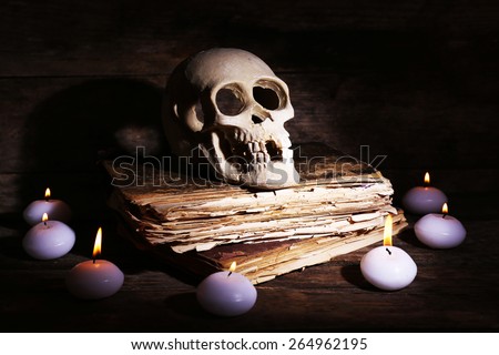 Still life with human skull, retro book and candlelight in dark on wooden table, closeup