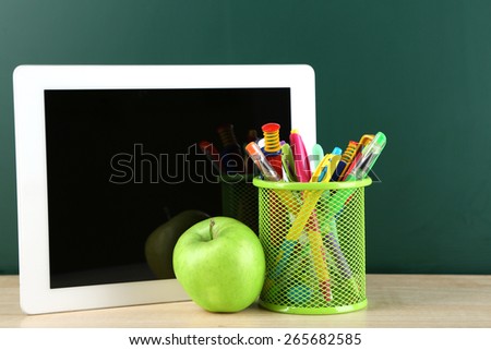 Digital tablet,  colorful pens and apple on desk in front of blackboard
