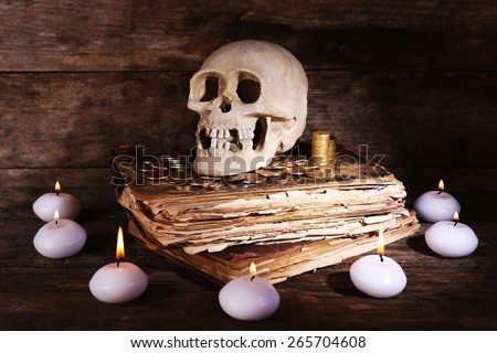 Still life with human skull, retro book and candlelight on wooden table, closeup