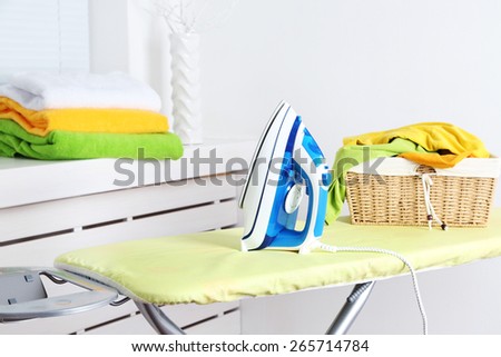 Iron and clothes on ironing board on interior background
