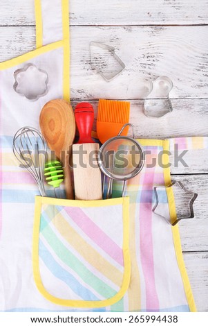Set of kitchen utensils in pocket of apron on wooden background
