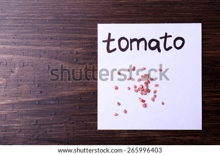 Tomato seeds on piece of paper on wooden background