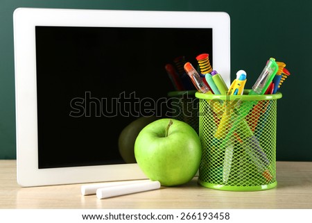 Digital tablet,  colorful pens and apple on desk in front of blackboard