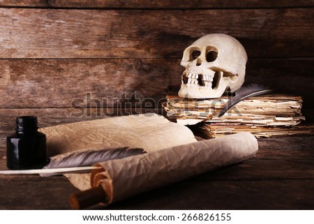 Still life with human skull, retro book and quill on wooden background