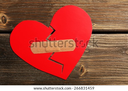 Broken heart with plaster on wooden background