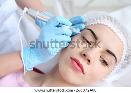 Cosmetologist applying permanent make up on eyes, close-up