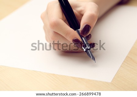 Female hand writing letter on white sheet of paper by fountain pen on wooden table background