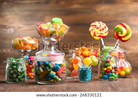 Colorful candies in jars on table on wooden background