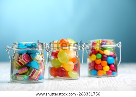 Colorful candies in jars on table on blue background background