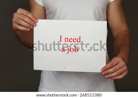 Sheet of paper with inscription I need a job in male hands on dark background