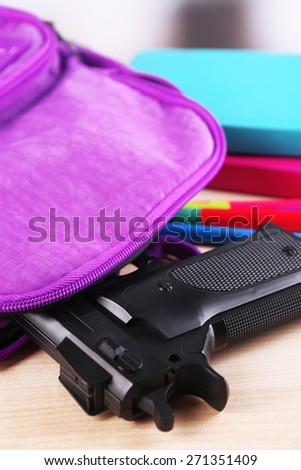 Gun in school backpack on wooden table, on bright background